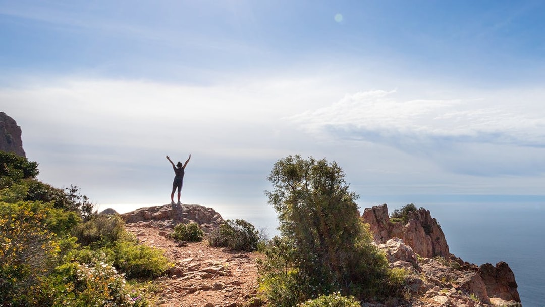 Hiker on rocky cliff overlooking sea at Massif de l'Esterel, France.