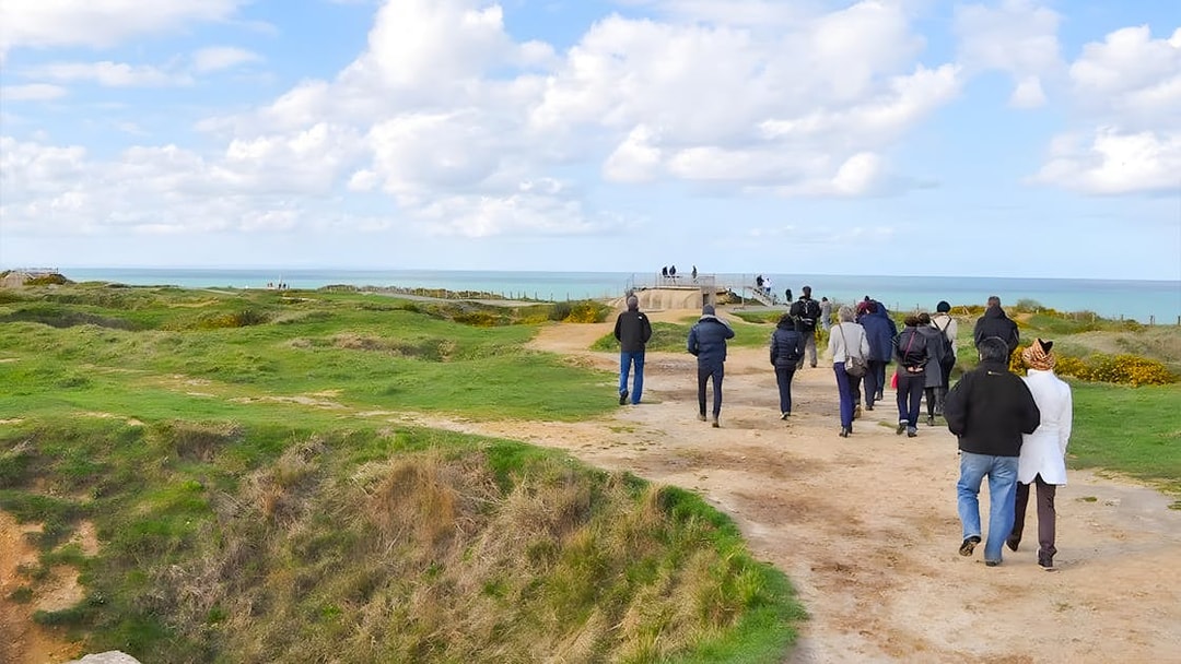 Tour group walking along Normandy beach cliffs with ocean view.