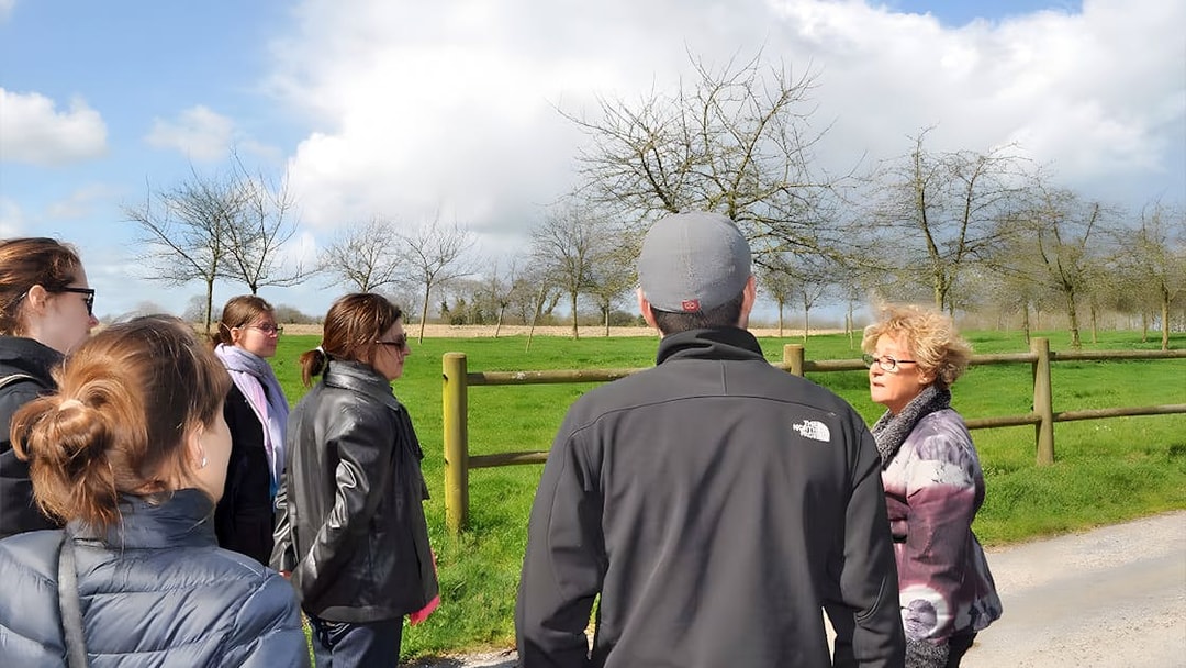 Tour group listening to a guide at Normandy, France, with green fields and trees in the background.