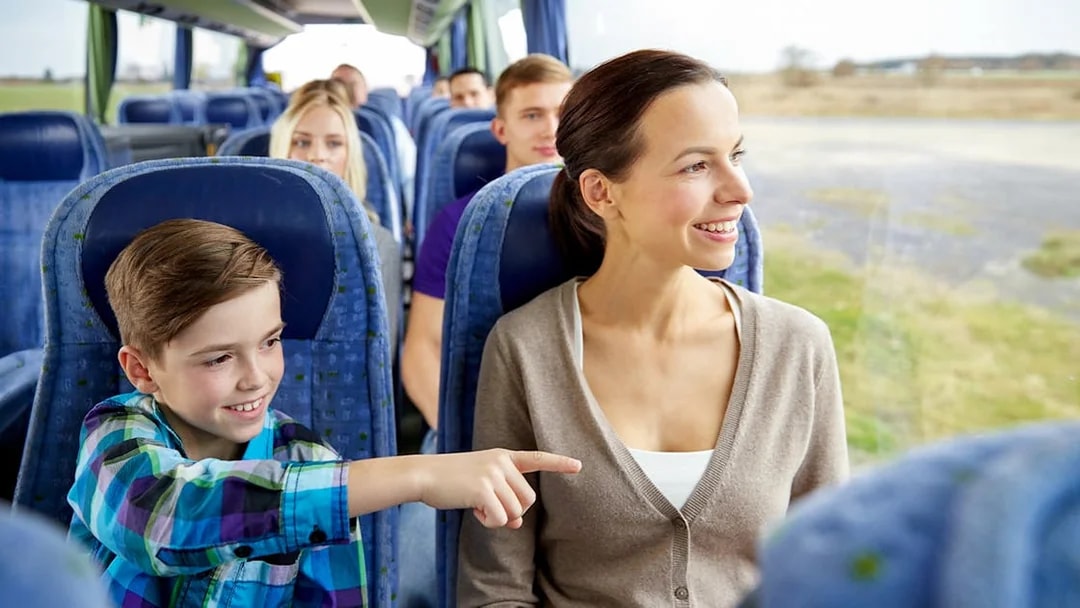 Woman and child smiling on a bus tour, looking out the window.