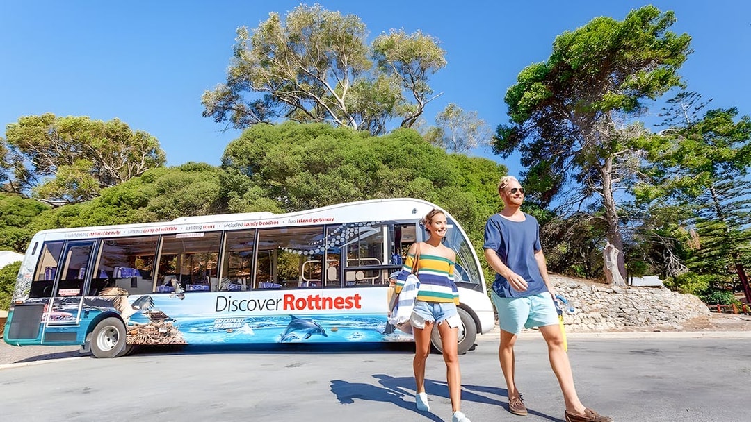 Tourists walking near a bus on Rottnest Island with coastal scenery in the background.