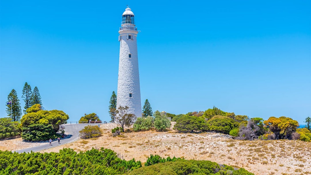 Rottnest Island lighthouse surrounded by trees under a clear blue sky.