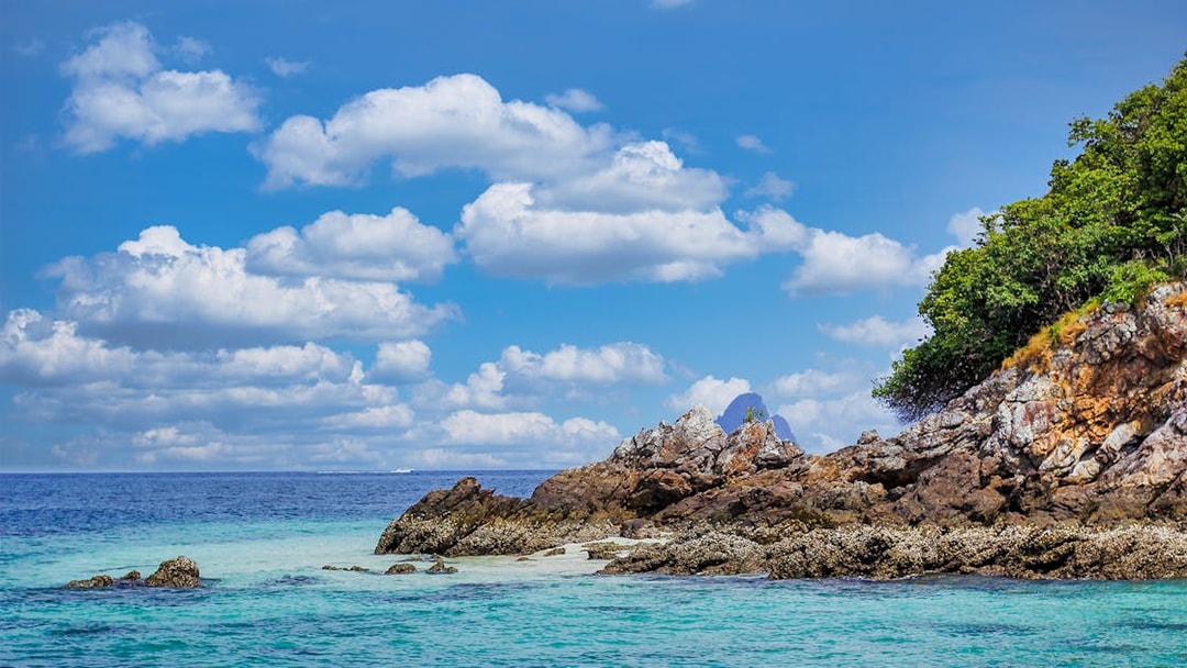 Rocky shoreline with clear blue water and lush greenery on Khai Nai Island, Thailand.