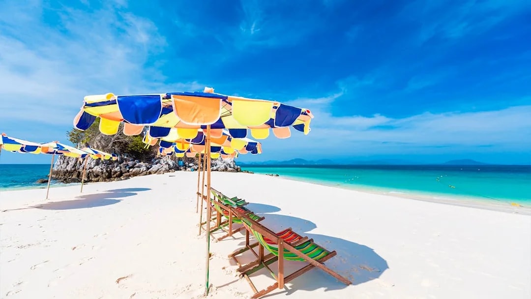 Colorful umbrellas and chairs on white sand beach in Khai Island, Thailand.
