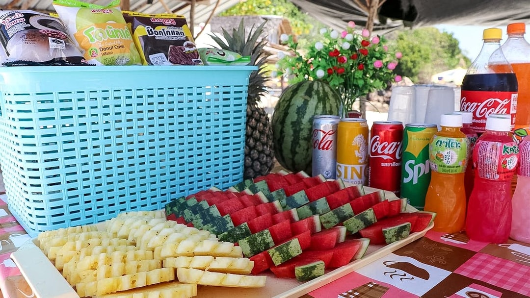 Snacks and drinks on a table at Khai Islands beach with sliced fruit and beverages.