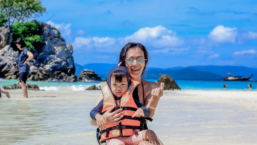 Mother and child in life vests enjoying Khai Island beach, Phuket, with clear blue water and rocks.