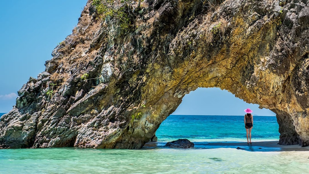 Person standing under rock arch by the sea on Khai Island.