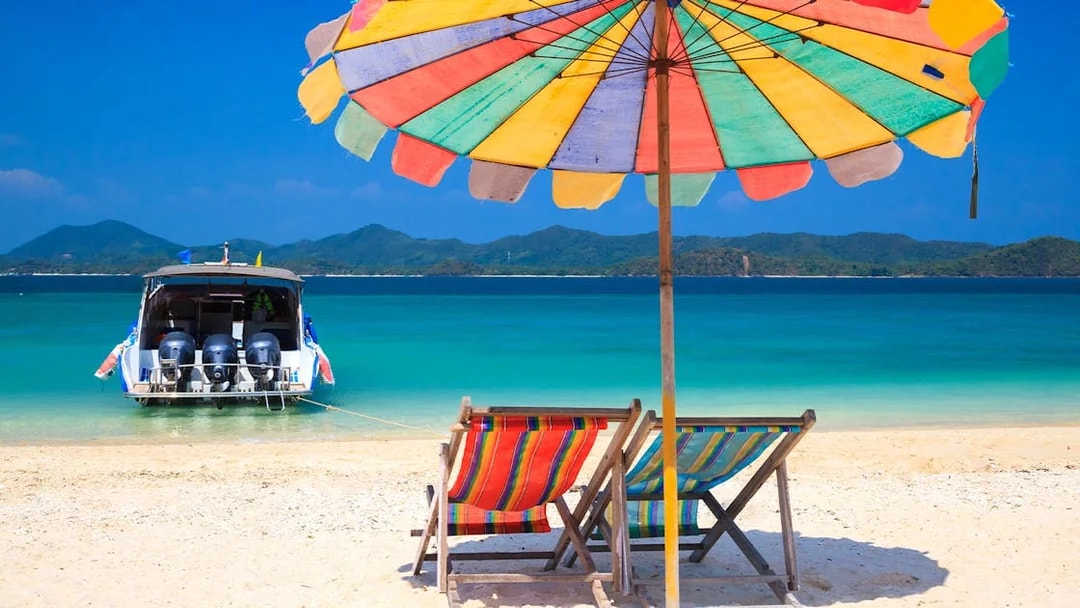 Beach chairs under umbrella facing boat on Koh Khai Island.