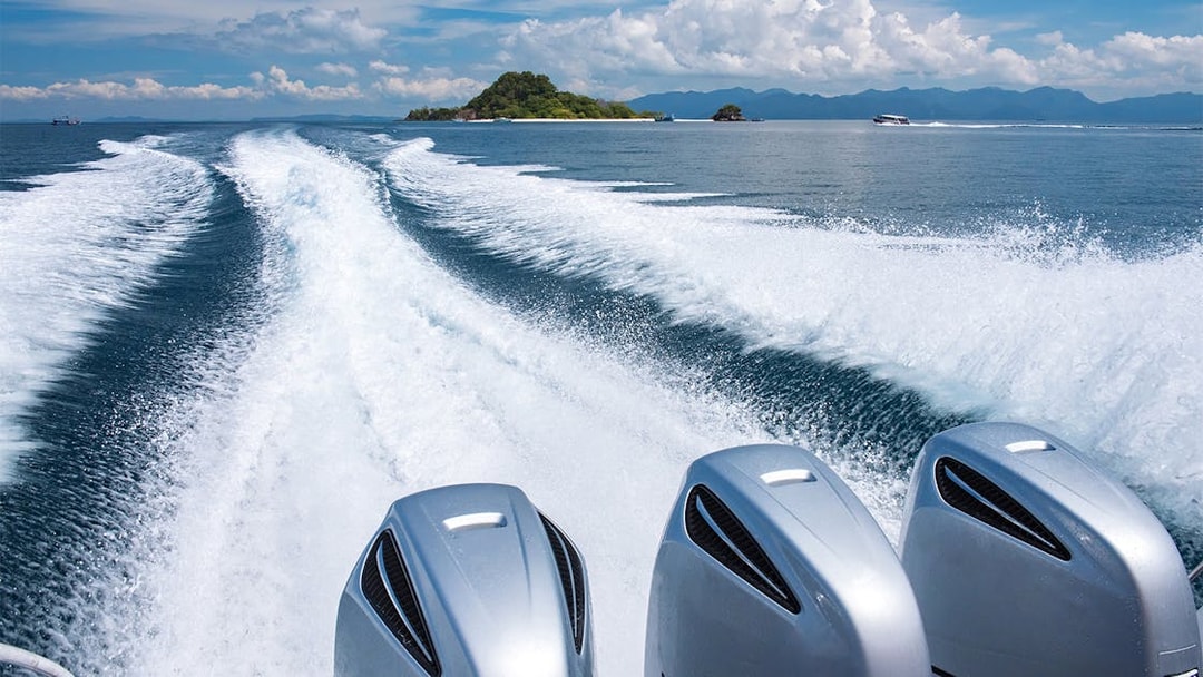 Speedboat leaving wake near Khai Islands, Phuket, with distant islands and clear sky.
