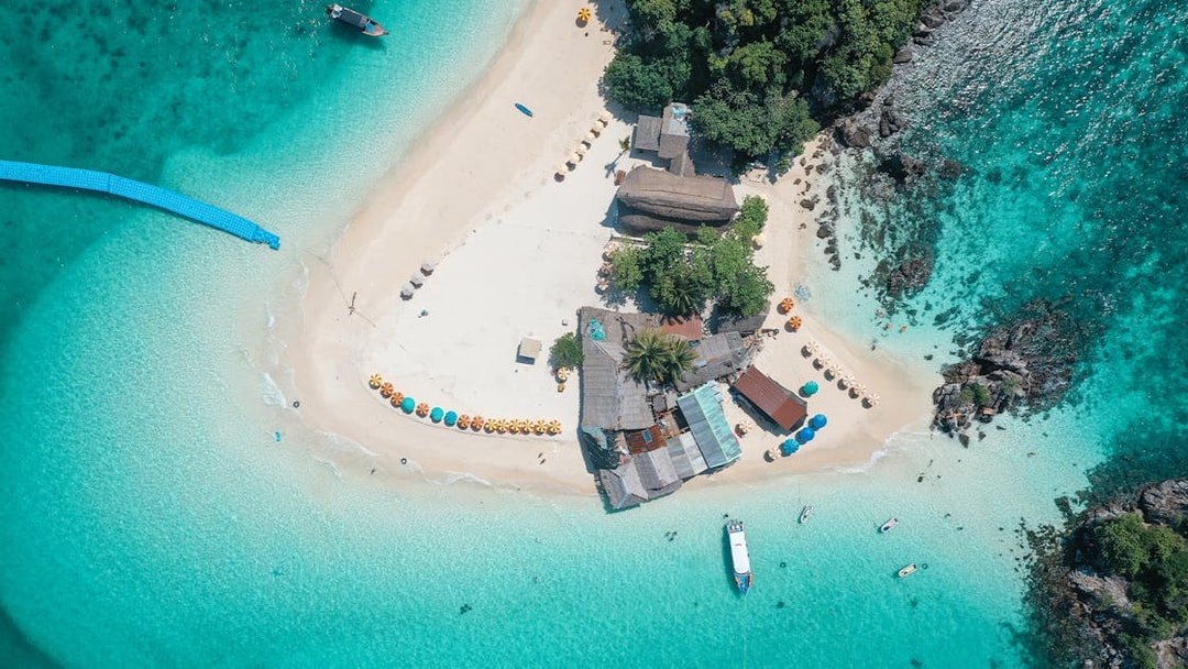 Aerial view of Khai Island beach with colorful umbrellas and speedboat in turquoise water, Phuket tour.