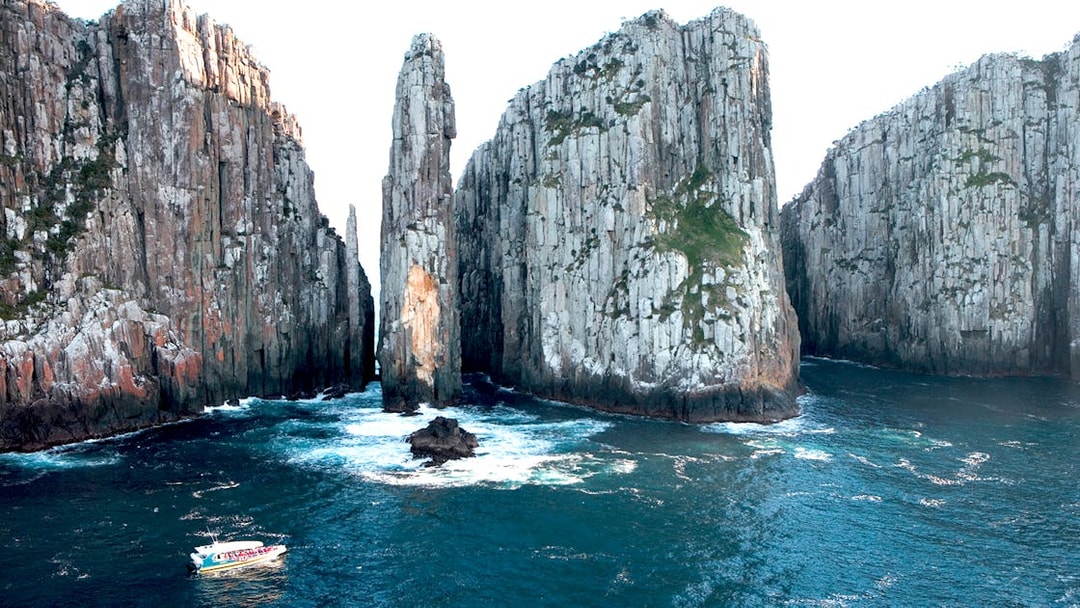 Cruise boat navigating between towering cliffs on Tasman Island, Australia.