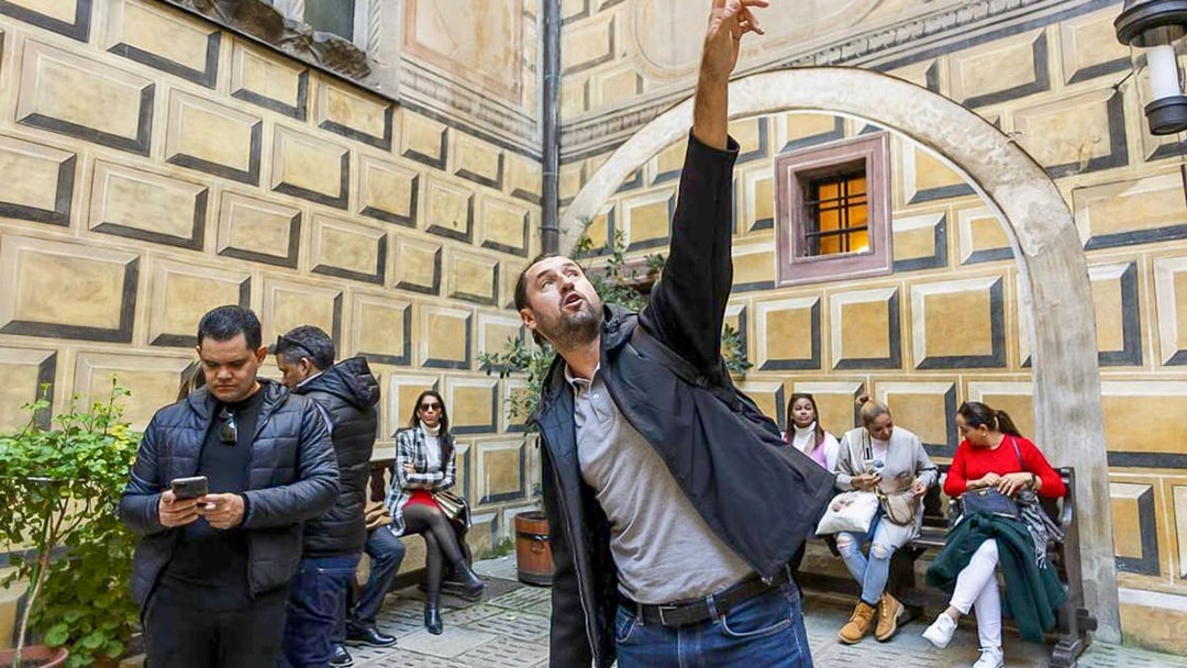 Tour guide pointing out architectural details in Cesky Krumlov courtyard.