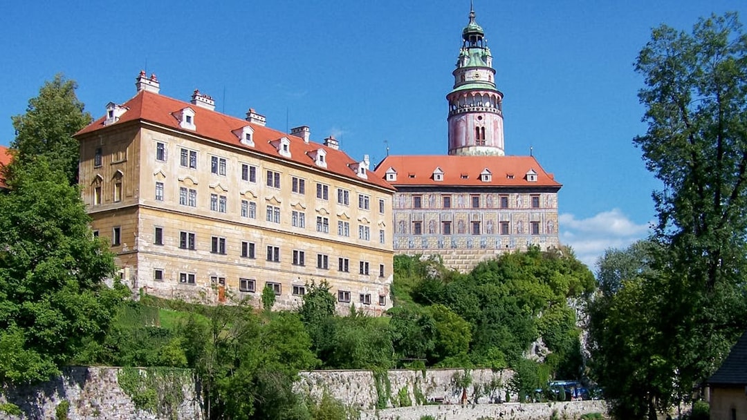 Cesky Krumlov Castle with red roofs and tower, surrounded by greenery.