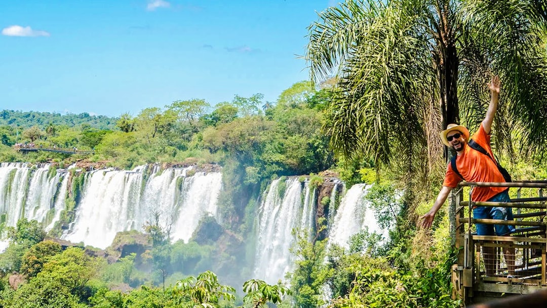 Tourist posing on a platform with Iguazu Falls in the background, Argentina.
