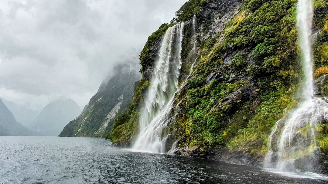 Waterfall cascading down lush cliffs in Doubtful Sound, New Zealand, viewed from a cruise.