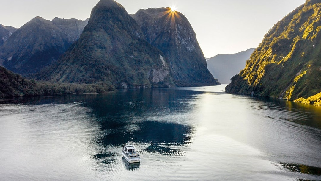 Cruise boat on Doubtful Sound with sunlit mountains, Queenstown tour.