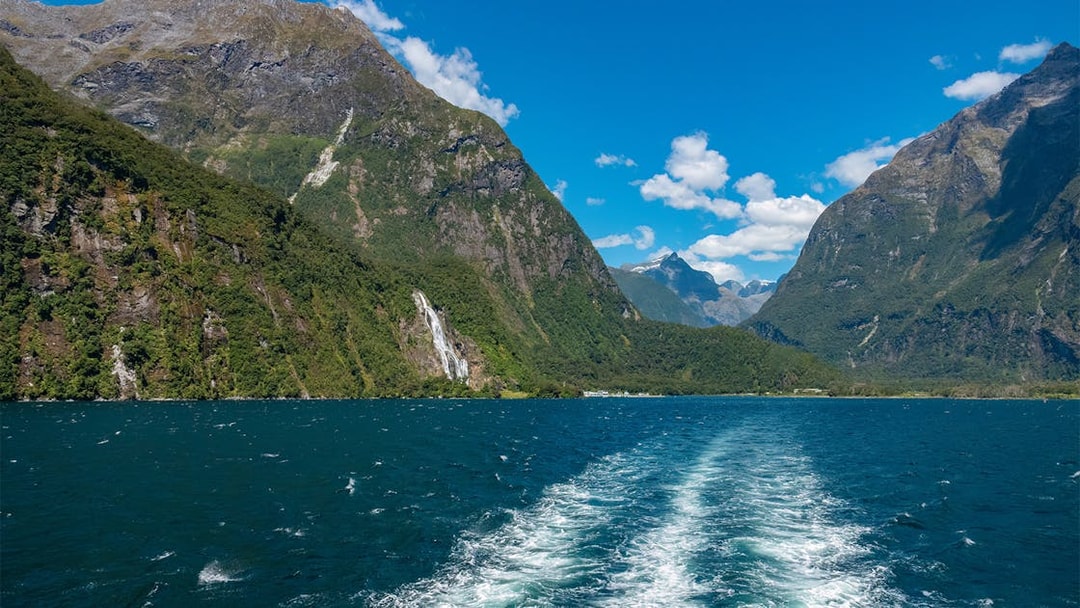 Doubtful Sound fjord with lush mountains and waterfall, seen from a cruise boat, New Zealand.