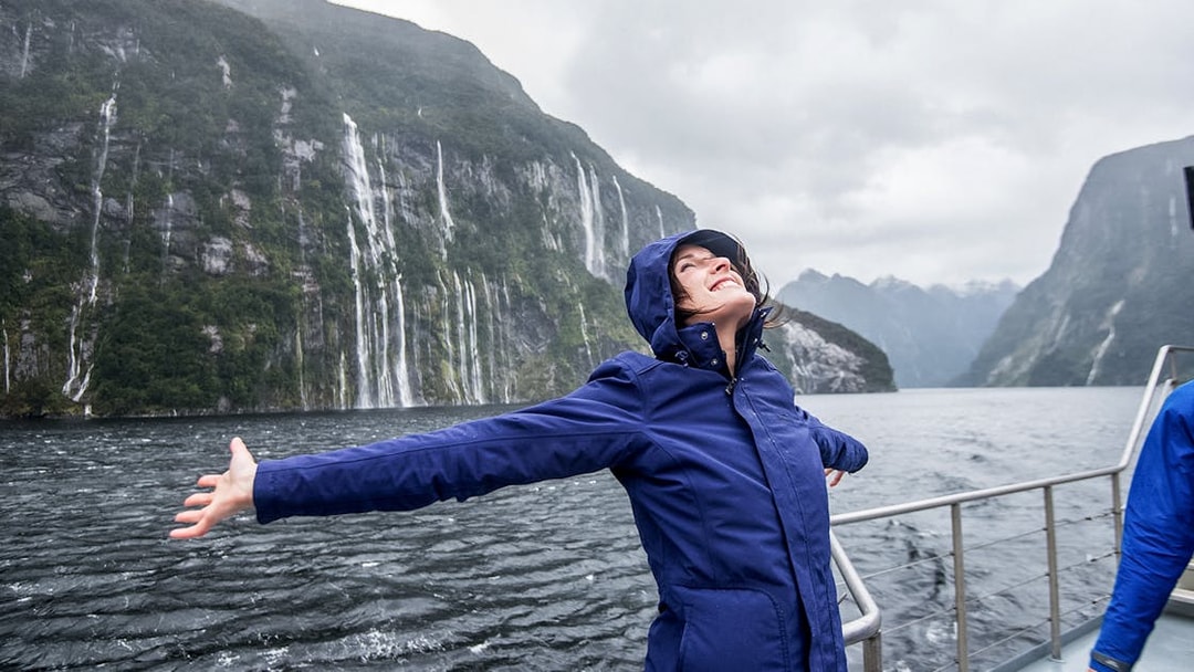 Person enjoying Doubtful Sound cruise with waterfalls and cliffs in the background, Queenstown.