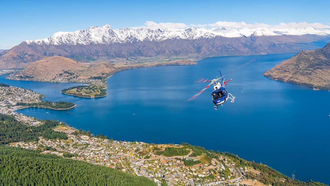 Helicopter flying over Lake Wakatipu with snow-capped mountains near Queenstown, New Zealand.