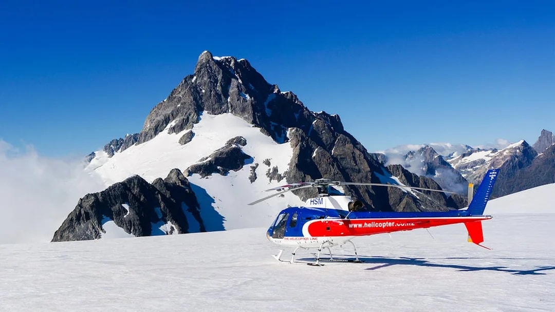 Helicopter on glacier with mountain backdrop, Milford Sound FlyCruiseHeli Tour.