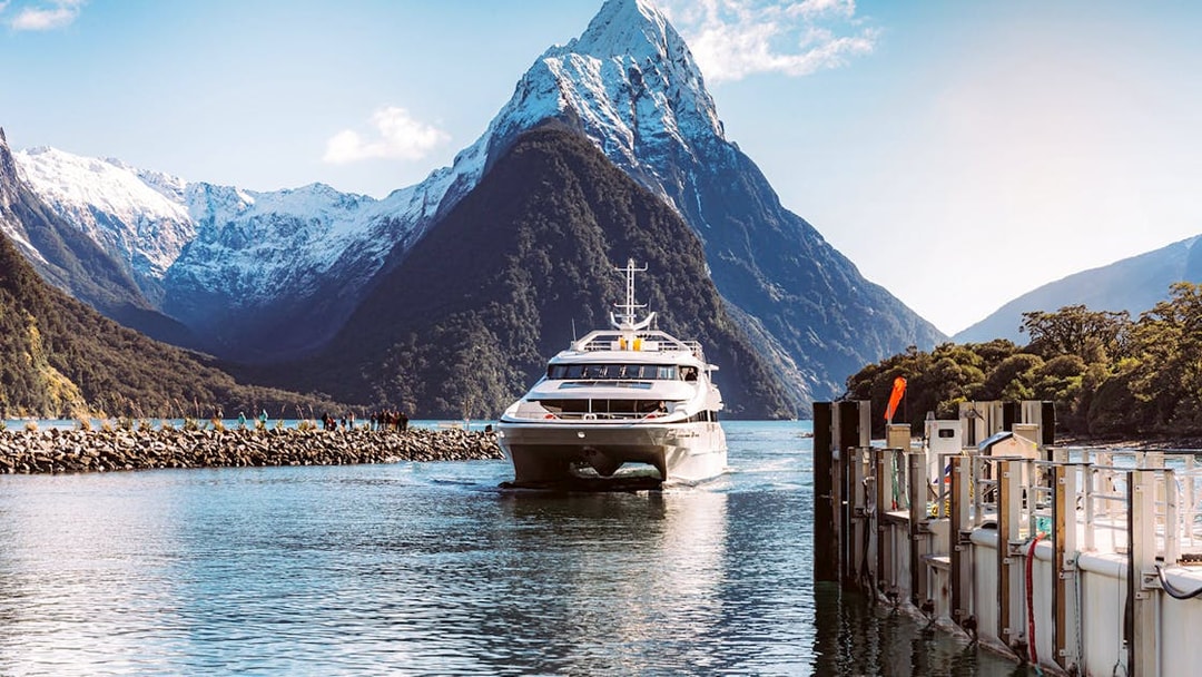 Cruise boat in Milford Sound with fjord views, lush mountains, and waterfalls, New Zealand.