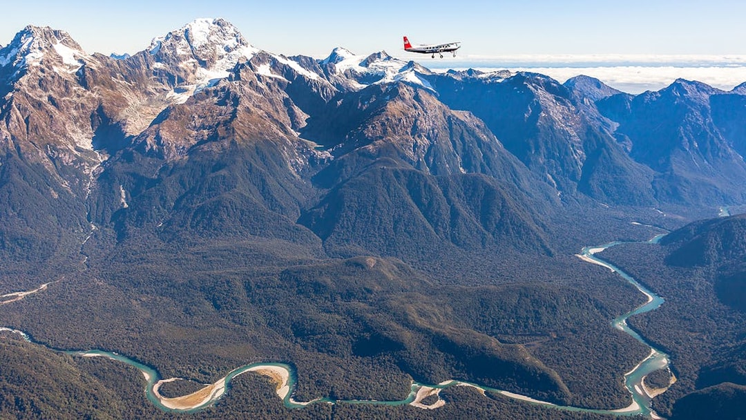 Aerial view of Milford Sound mountains with a plane flying over, showcasing scenic flyover from Queenstown.