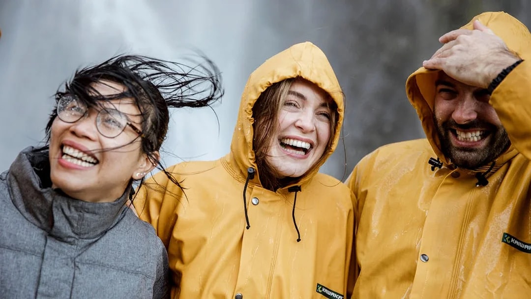 Tourists in raincoats smiling near a waterfall on Milford Sound day trip from Queenstown.