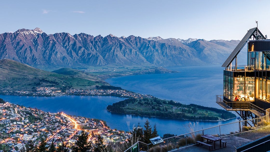 Aerial view of Queenstown with Lake Wakatipu and surrounding mountains at sunset.