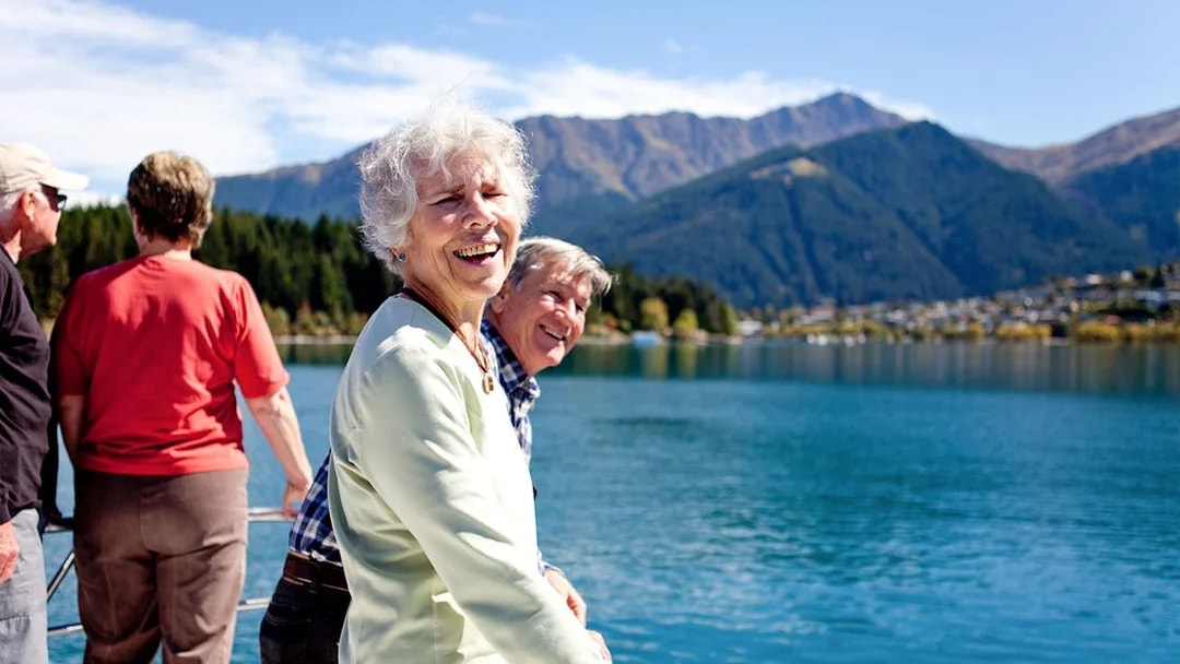 Senior passengers enjoying mountain views on Lake Wakatipu boat cruise in Queenstown.