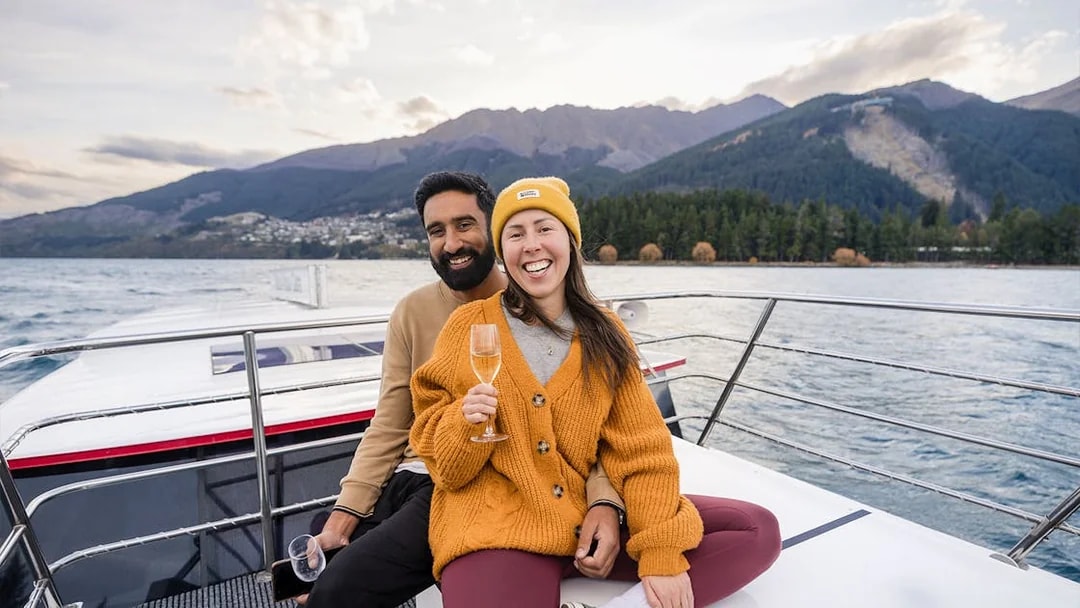 Couple enjoying wine on a boat with Queenstown mountains in the background on Lake Wakatipu.