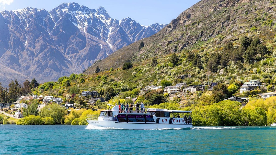 Cruise boat on Lake Wakatipu with passengers viewing Queenstown's Remarkables mountains.