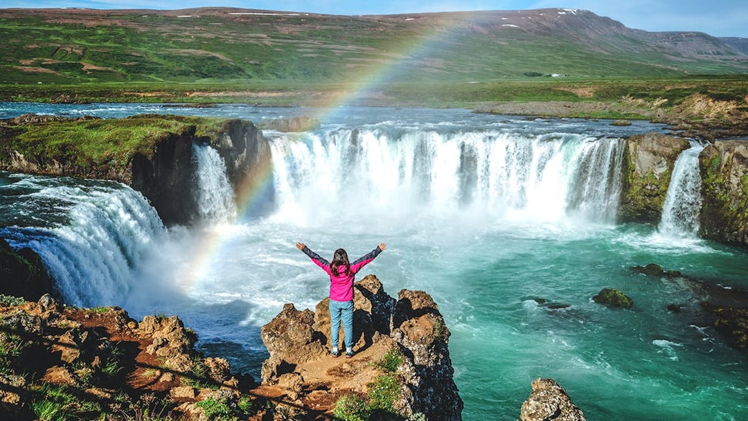 Tourist at Gullfoss waterfall in Iceland with a rainbow overhead.