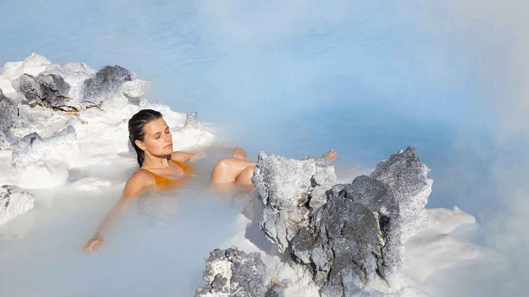 Tourist relaxing in Blue Lagoon, Iceland, surrounded by geothermal rocks.