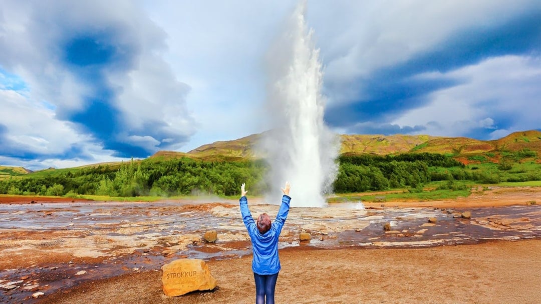 Woman raising arms near erupting Strokkur Geyser, Iceland.