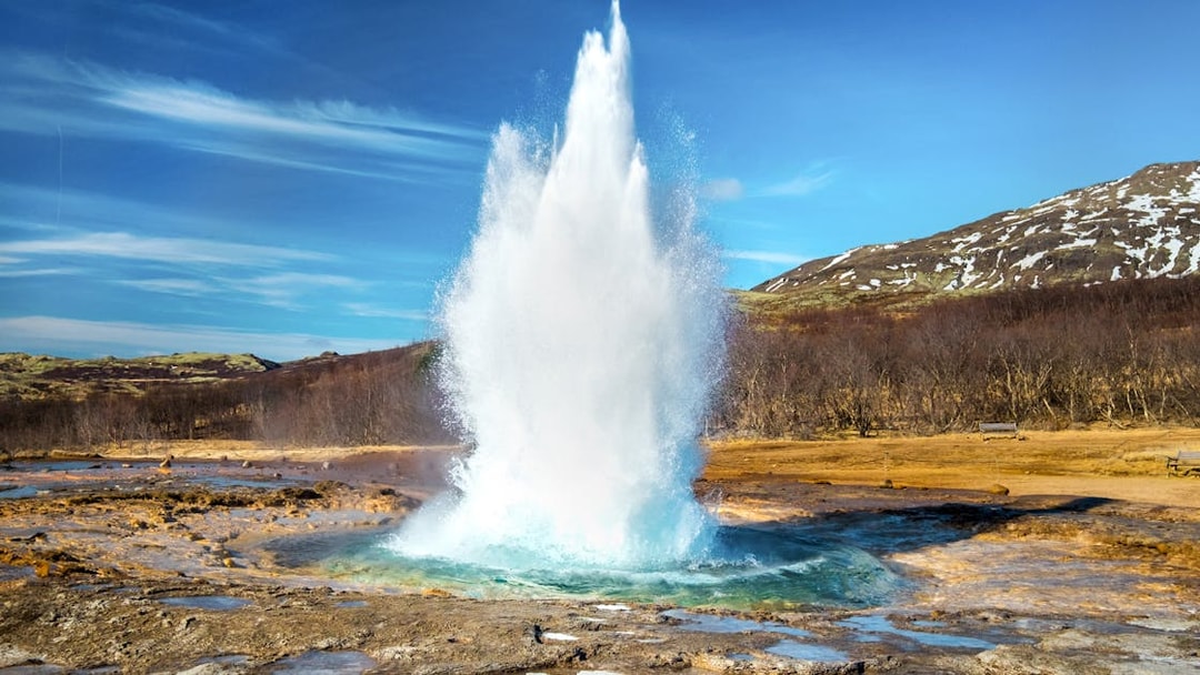 Geyser erupting in the Golden Circle, Iceland with snowy hills in the background.