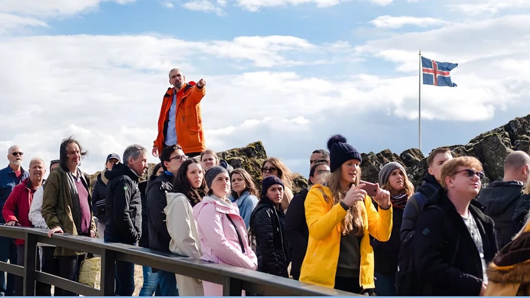 Tour group with guide at Thingvellir National Park, Icelandic flag in background.