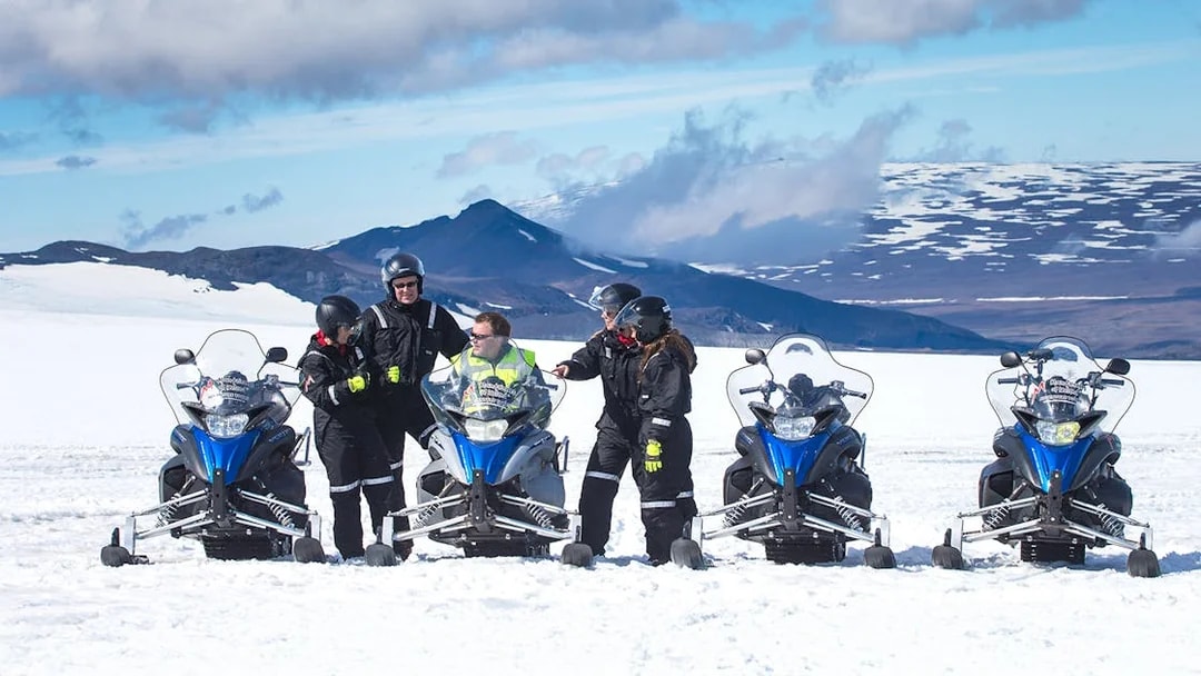 Snowmobile riders on Langjokull Glacier with snowy mountains in the background.