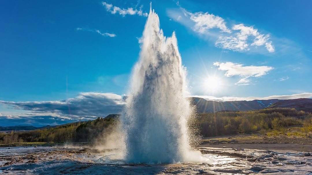 Strokkur geyser erupting under a clear sky in Iceland's Golden Circle tour.