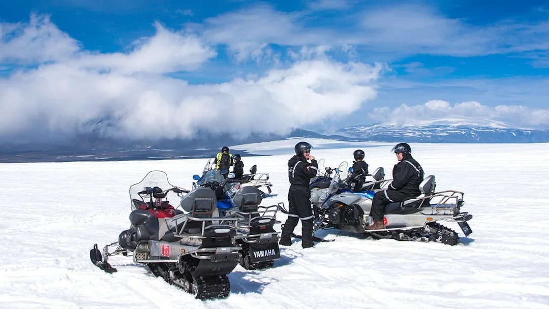 Snowmobile riders on Langjokull Glacier, Iceland, with snowy landscape and blue sky.