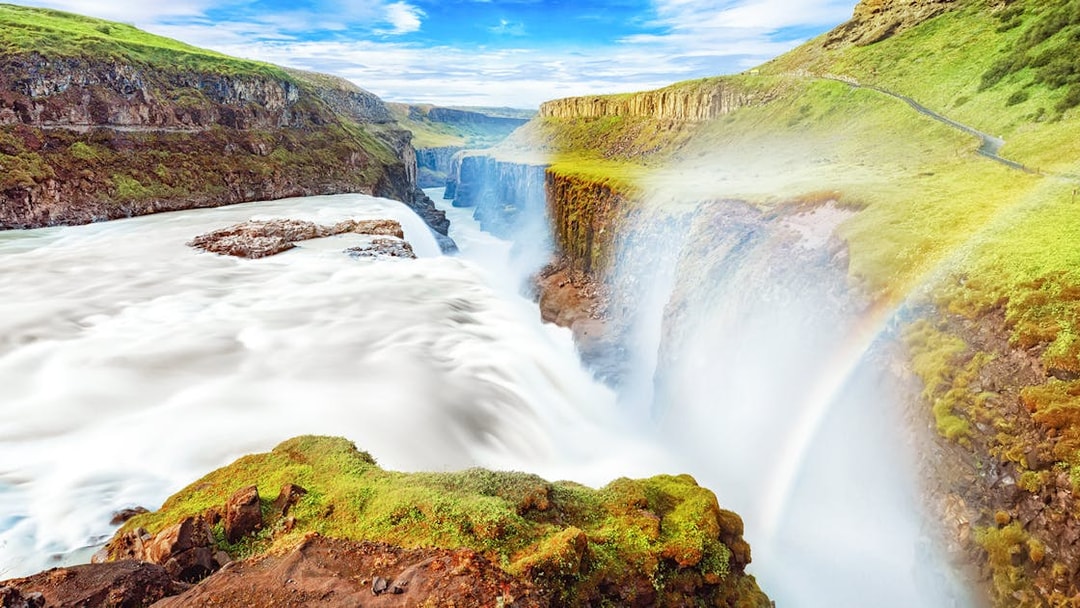 Gullfoss waterfall cascading over rocky cliffs in Iceland with a rainbow.