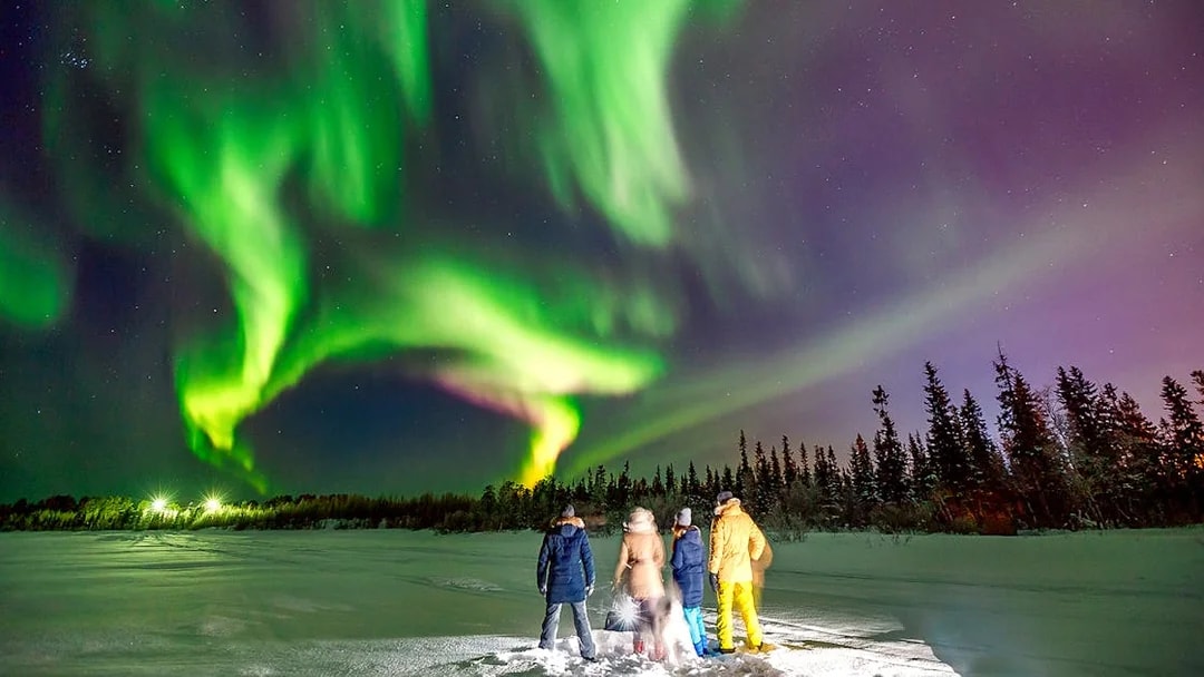 Tourists watching Northern Lights on a snowy landscape during a small group tour.