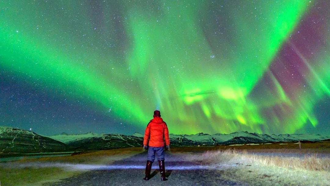 Tourist in red jacket watching northern lights in Norway.