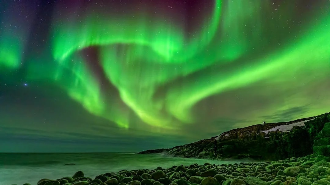 Northern Lights over rocky coastline in Iceland.