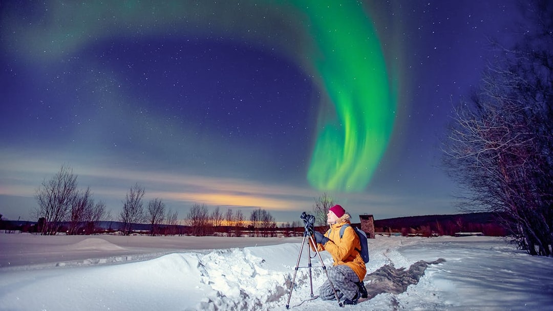 Person photographing Northern Lights on snowy landscape during Premium Small Group Northern Lights Tour.
