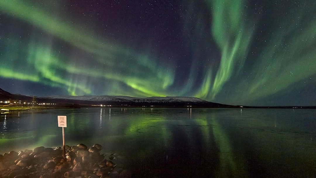 Northern Lights over a calm lake with distant snowy mountains in Iceland.