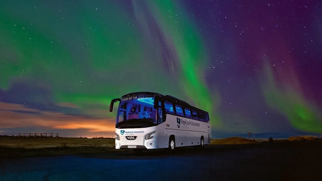 Tour bus under Northern Lights in Iceland's night sky.