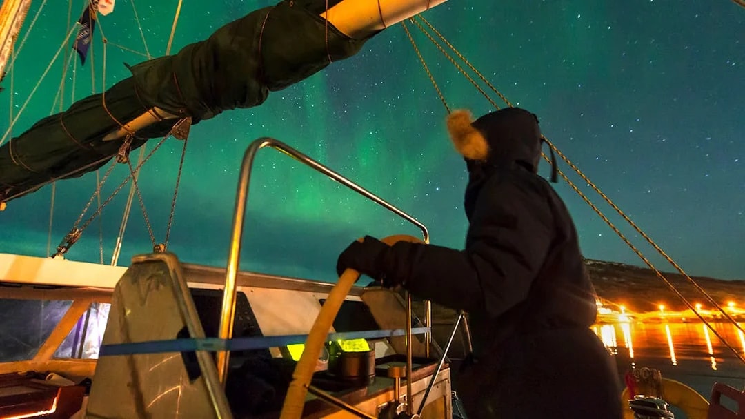 Person steering a boat under the Northern Lights near Reykjavik.