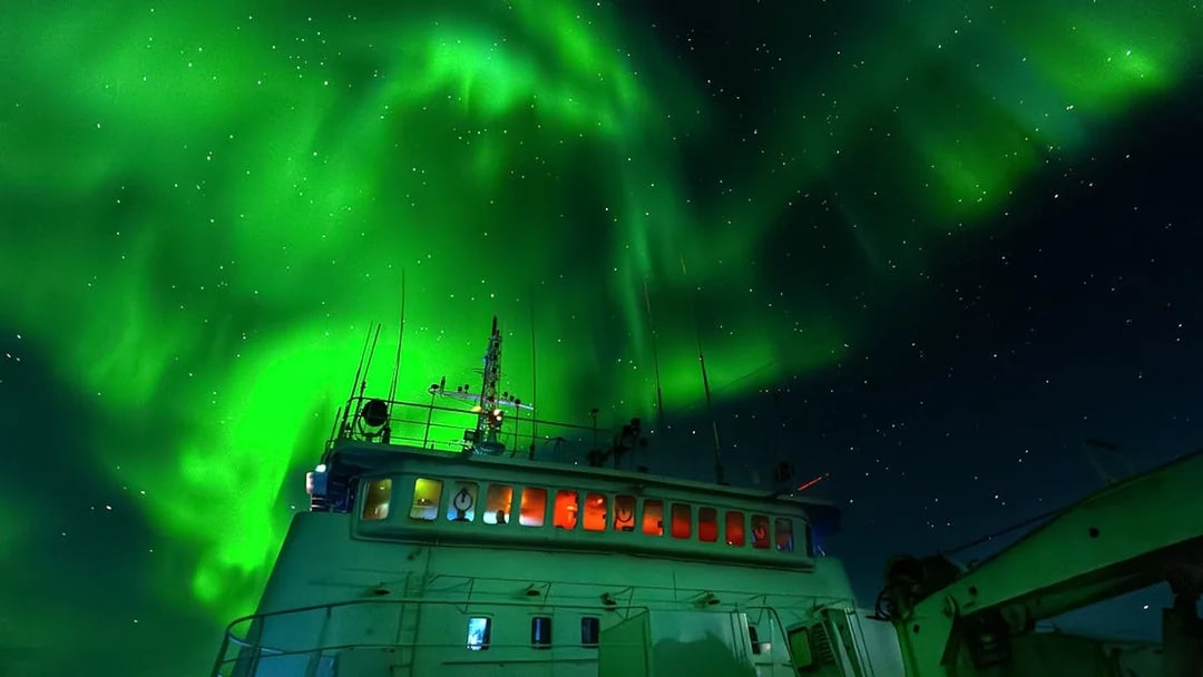 Cruise ship under Northern Lights in Reykjavik night sky.
