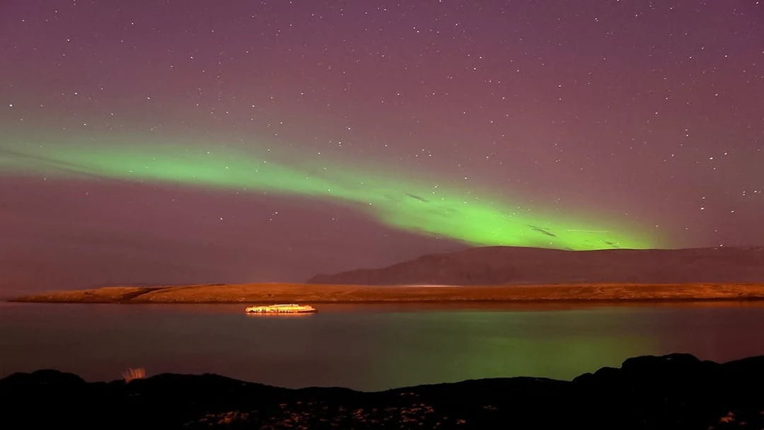 Northern Lights over water with a cruise ship near Reykjavik.