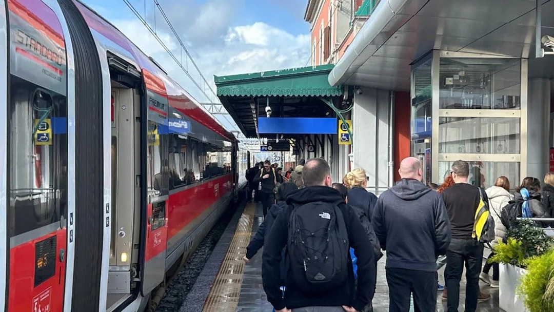 Passengers walking along a platform beside a red train at a station.